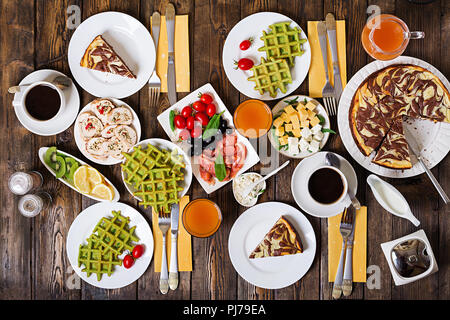 Frühstück in der Tabelle. Festlicher brunch, essen Vielzahl mit Spinat Waffeln, Lachs, Käse, Oliven, chicken Rolls und Käsekuchen. Ansicht von oben. Flach Stockfoto