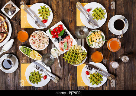 Frühstück in der Tabelle. Festlicher brunch, essen Vielzahl mit Spinat Waffeln, Lachs, Käse, Oliven, chicken Rolls und Käsekuchen. Ansicht von oben. Flach Stockfoto