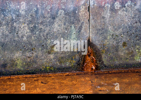 Zwei Betonplatten von schmutzig grauen Farbe in Spots, rostiges Wasser fließt aus dem Loch von unten, im Vordergrund Es ist ein flüssiges Rusty von Korrosion, Stockfoto