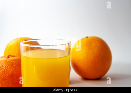 Glas Saft mit drei Mandarinen auf weißem Hintergrund. Nahaufnahme Foto. Stockfoto