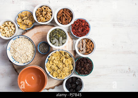 Zutaten für ein gesundes Müsli: Nüsse, Hafer, Getreide und Getreideerzeugnisse und getrocknete Früchte auf dem weißen Holz- Tabelle, Ansicht von oben, selektiver Fokus, kopieren Raum Stockfoto