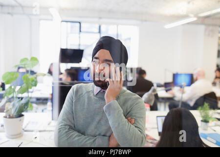 Ernsthafte indischer Geschäftsmann in Turban auf Smart Phone im Büro Stockfoto