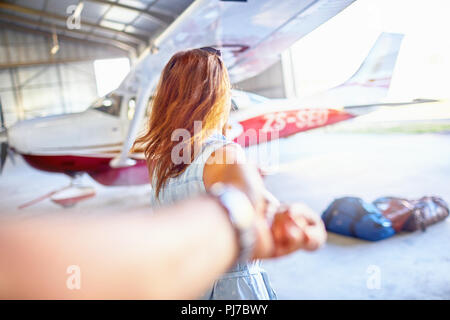 Persönliche Perspektive Frau führenden Mann an der Hand zu kleinen Flugzeug im Hangar Stockfoto