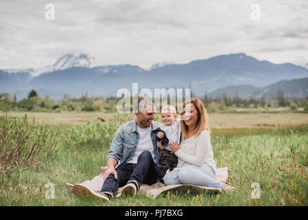 Eltern und Baby Sohn sitzen im ländlichen Gebiet mit Bergen im Hintergrund Stockfoto