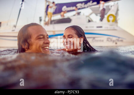 Glückliche junge erwachsene Paare schwimmen in der Nähe von Katamaran in Ocean Stockfoto