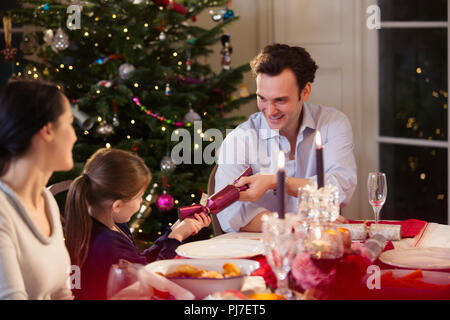 Vater und Tochter ziehen Christmas Cracker bei candlelight dinner Tabelle Stockfoto