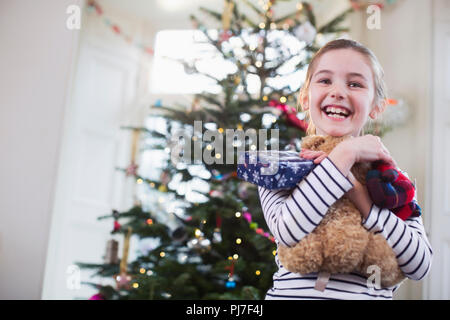 Porträt Lächeln, süße Mädchen umarmt Teddybär vor Weihnachtsbaum Stockfoto