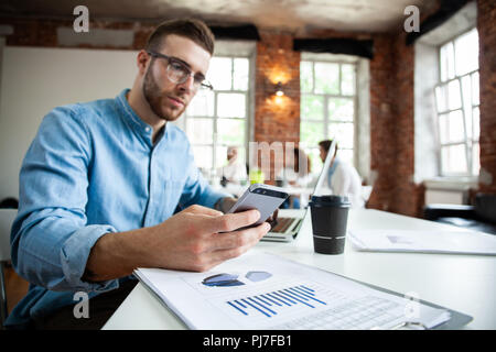 Arbeitsbereich lifestyle Konzept. Geschäftsmann mit Smartphone. Gut aussehender Geschäftsmann ist mit einem Smartphone und lächelnd, während im Büro arbeiten Stockfoto