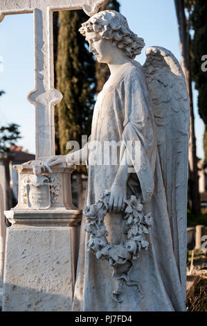 Ein Marmor Engel mit seiner Hand auf das Kreuz, unter den Gräbern des Friedhofs, bei der Konzentration, hält einen Kranz Stockfoto