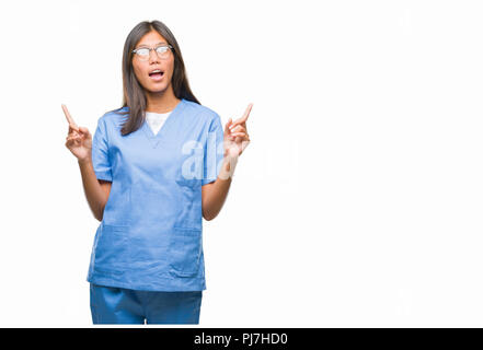 Jungen asiatischen Arzt Frau über isolierte Hintergrund erstaunt und überrascht mit der Suche und zeigt mit Fingern und erhobenen Armen. Stockfoto