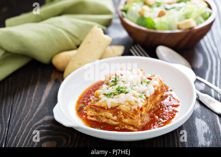 Traditionelle Lasagne auf weiße Platte mit Caesar Salat und Grissini Stockfoto