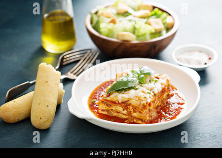 Traditionelle Lasagne auf weiße Platte mit Caesar Salat und Grissini Stockfoto
