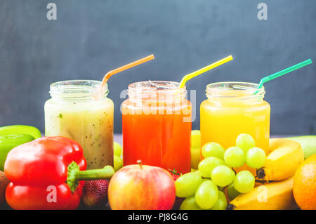 Frisch gepresste Fruchtsäfte, Smoothies gelb orange grün Banane Zitrone Apfel Orange kiwi Trauben Erdbeere auf einem dunklen Hintergrund Platz kopieren Stockfoto