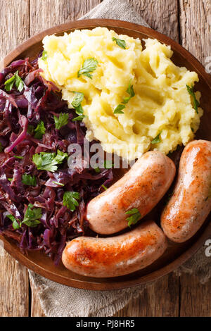 Deutsche Küche: Kartoffelpüree, gedünstetem Rotkohl und Würstchen close-up auf einem Teller. Vertikal oben Ansicht von oben Stockfoto