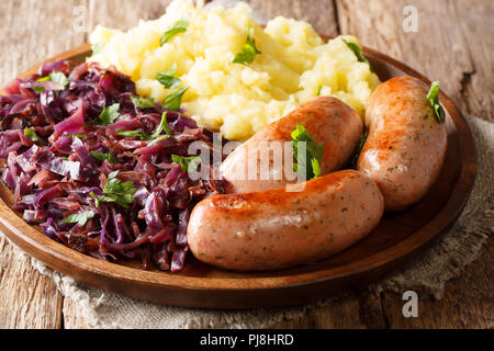 Gebratene Würstchen mit Sauerkraut und Kartoffeln close-up auf einem Teller auf dem Tisch. Horizontale Stockfoto