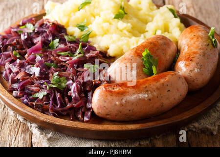 Mittagessen, Kartoffelpüree mit gedünstetem Rotkohl und gebratene Würstchen close-up auf einem Teller auf den Tisch. Horizontale Stockfoto