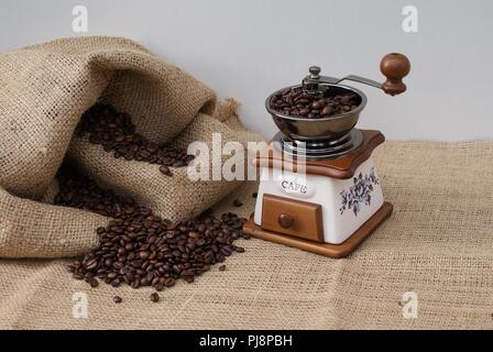 Alte Kaffeemühle gefüllt mit Kaffeebohnen neben einem Kaffee Sack Stockfoto