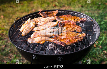 Die schweinekoteletts und hähnchenspieße am Grill zubereitet. Die Zubereitung von Fleisch und Grillen auf direkte Wärme in der Natur im Hinterhof BBQ-Picknick. Stockfoto