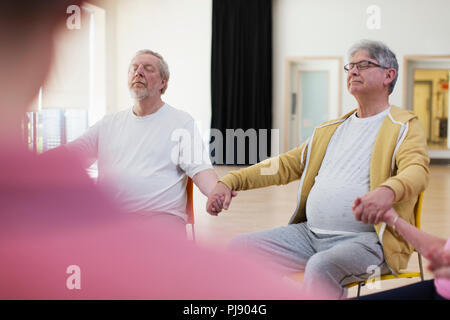 Serene aktive ältere Männer halten sich an den Händen, meditieren im Community Center Stockfoto