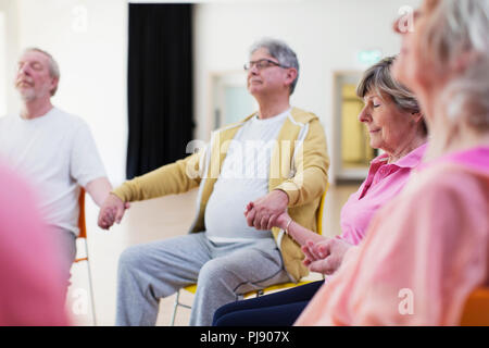 Serene aktive Senioren halten sich an den Händen, meditieren Stockfoto