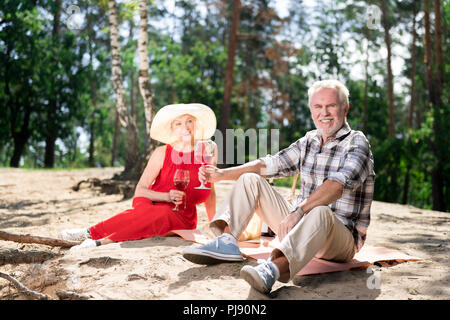 Paar strahlende ältere Frau und Mann sitzen auf Sand in Picknick Stockfoto