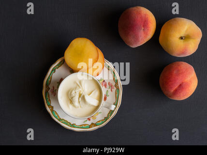 Pfirsiche, ganz und geschnitten und Sahne in die Tasse auf schwarzem Hintergrund - Ansicht von oben Foto Stockfoto