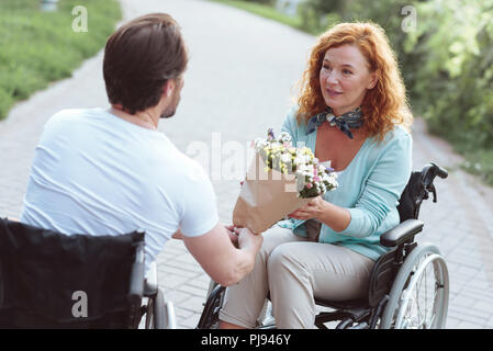 Erstaunt, Frau im Rollstuhl Blumen von Freund Stockfoto