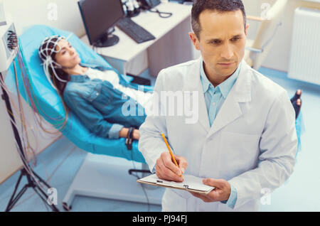 Schwere Arzt Notizen während der elektroenzephalographie Verfahren Stockfoto
