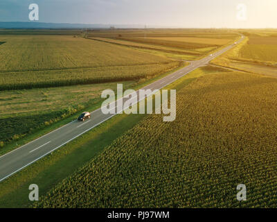 Luftaufnahme von zweispurigen Autobahn Straße durch Landschaft und kultivierten Feld von Mais im Sommer Sonnenuntergang Stockfoto