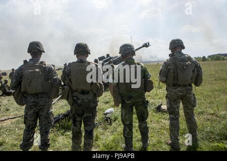 Militärisches Personal aus verschiedenen Nationen beobachten, wie US-Marines mit Echo. Akku, 2. Bataillon, 10 Marine Regiment (2/10), 2nd Marine Division Feuer ein M777 Haubitze in Salisbury, England, Juli 5, 2018. Marines mit der Unit durchgeführt live-fire Übungen mithilfe der M777 Haubitze während der Übung grüne Kanone 18. Grüne Kanone ist eine multinationale Übung mit US-Marines die Möglichkeit, Taktiken und Techniken sowie zu Exchange Projekt Letalität und Combat Power auf der ganzen Welt neben Partner Nationen. Stockfoto