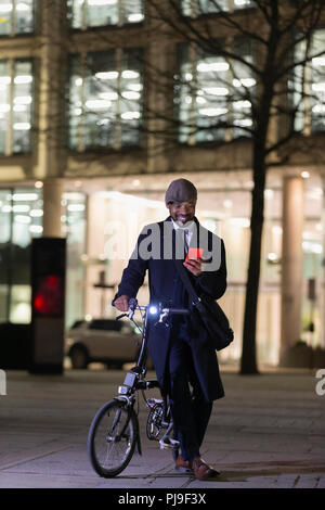 Geschäftsmann mit Hilfe smart phone Fahrrad auf städtischen Gehsteig in der Nacht Stockfoto