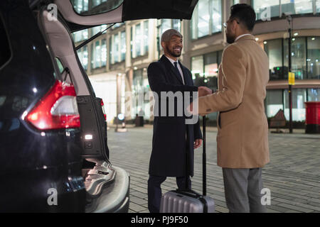 Geschäftsmann mit Koffer handshaking an der Rückseite des Auto auf Urban Street bei Nacht Stockfoto