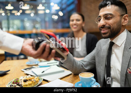 Unternehmer zahlen mit smart phone kontaktloses Bezahlen im Café Stockfoto