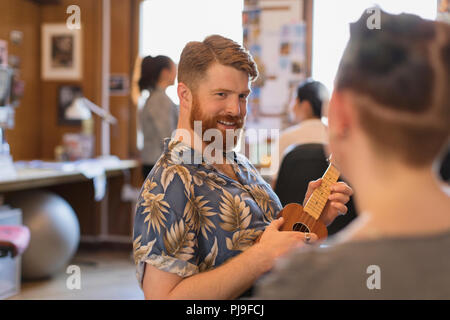 Lächelnde kreative Geschäftsmann spielen Ukulele im Büro Stockfoto