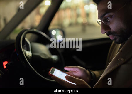 Mann mit smart Telefon im Auto in der Nacht Stockfoto