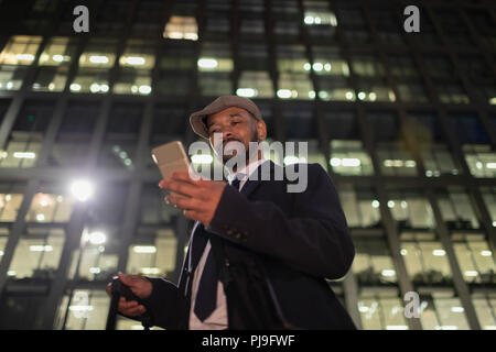 Geschäftsmann mit smart phone stehen unter städtischen Hochhaus in der Nacht Stockfoto