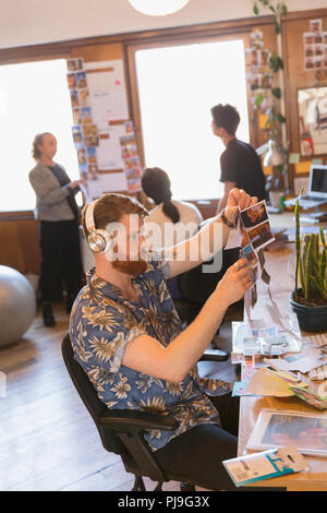 Kreative männlichen Designer mit Kopfhörer überprüfen Foto Beweise im Büro Stockfoto
