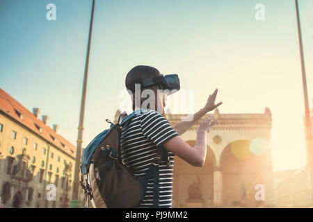 Mädchen Tourist in Gläser der Virtuellen Realität. Virtuelle Reise nach Deutschland. Das Konzept der virtuellen Tourismus. Im Hintergrund ist der Platz auf der Leopoldstraße in München. Stockfoto