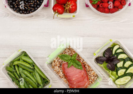 Kunststoff Mahlzeit prep Container grüne Erbsen, mit gekochten Buchweizen Brei und Scheiben von Fleisch, frischen Gurken und Salat, Johannisbeere, Erdbeere, Himbeere Stockfoto