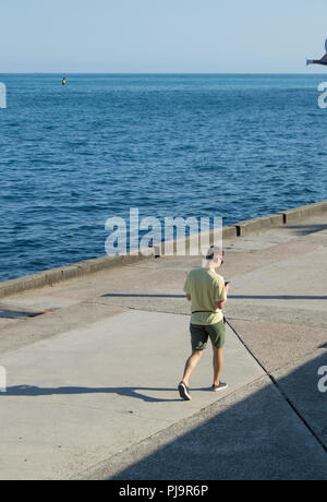 Moderne modische junge Mann allein zu Fuß an der Strandpromenade, an Ihrem Gerät suchen Stockfoto