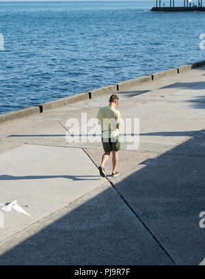 Moderne modische junge Mann allein zu Fuß an der Strandpromenade, an Ihrem Gerät suchen Stockfoto