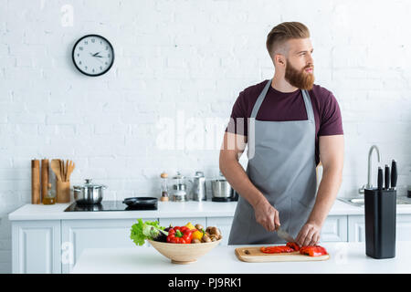 Gut aussehender bärtiger junger Mann in Schürze weg schauen, beim Kochen in der Küche Stockfoto