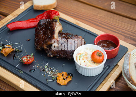 Köstliches saftiges BBQ Schweinerippchen mit Krautsalat Salat auf Schneidebrett serviert. Stockfoto