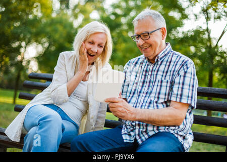 Gerne älteres Paar wird mit Hilfe von digitalen Tablette im Park. Stockfoto