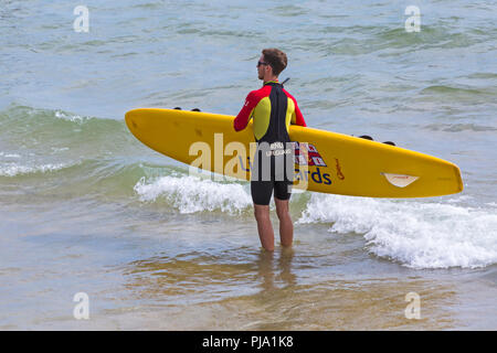 RNLI Rettungsschwimmer hält Surfbrett am Strand von Bournemouth, Bournemouth, Dorset UK im September Stockfoto