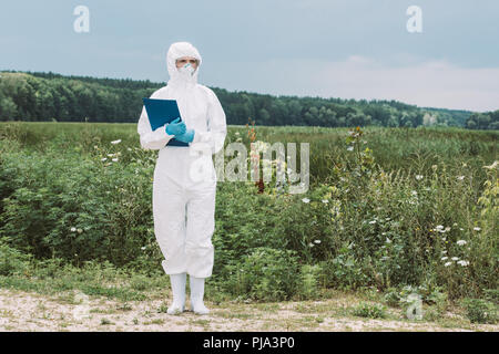 Wissenschaftlerin in Schutzanzug und Googles holding Zwischenablage in der Wiese Stockfoto