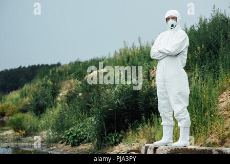 Männliche Wissenschaftler in Schutzanzug und Maske in der Nähe von Wasser im Freien Stockfoto