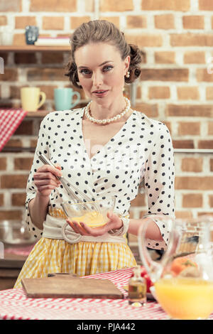 Attraktive nach hausfrau Rühren für Eier, Omelette und Kamera in Küche Stockfoto
