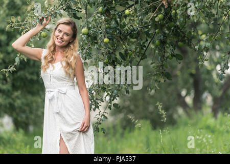 Gerne stilvolle Frau in weißem Kleid im Obstgarten mit Apfelbäumen posing Stockfoto