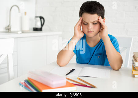 Portrait der fokussierten Junge sitzt am Tisch mit copybook, Pen und Notebooks zu Hause Stockfoto
